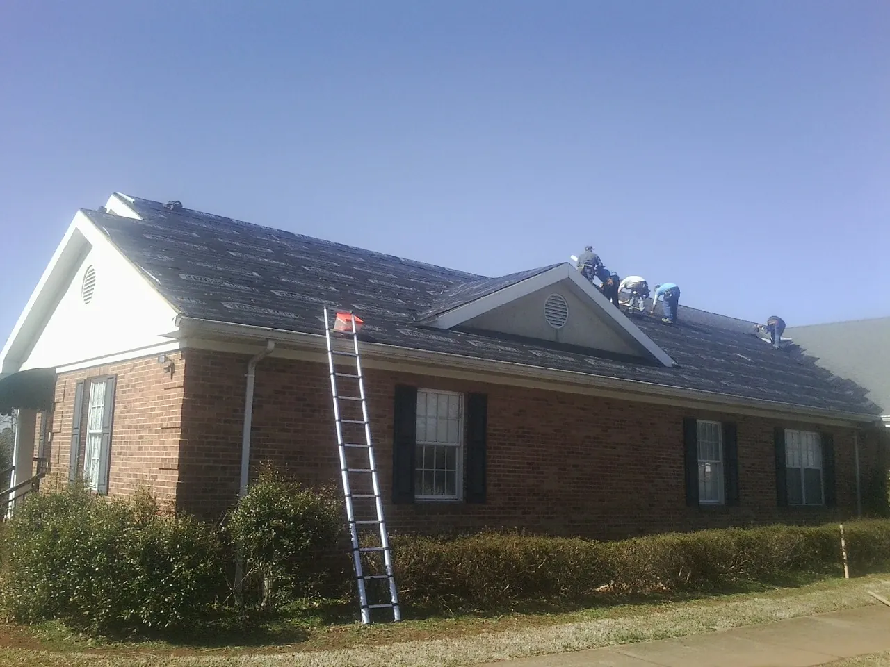 Crew tearing shingles off a brick ranch roof with a ladder set — Metal Roof Repair work by our crew in Pittsboro