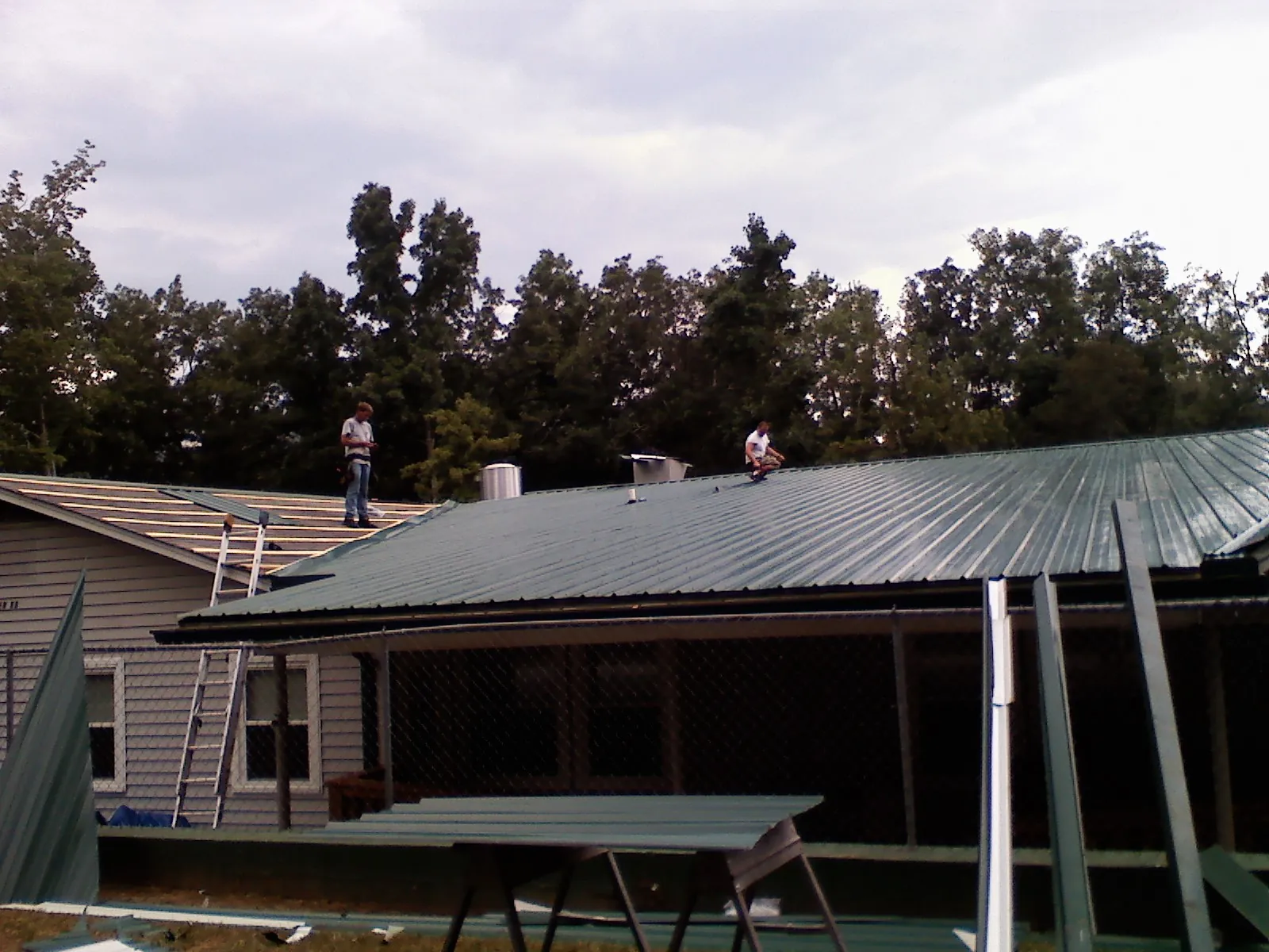 Two roofers installing green metal panels above a covered porch in Pittsboro
